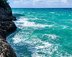 blue ocean waves next to rocky hill